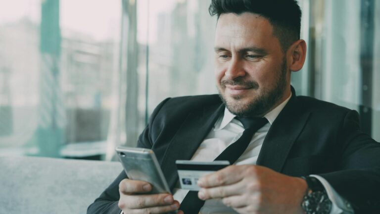 A businessman uses a smartphone and credit card for online shopping in an office setting.
