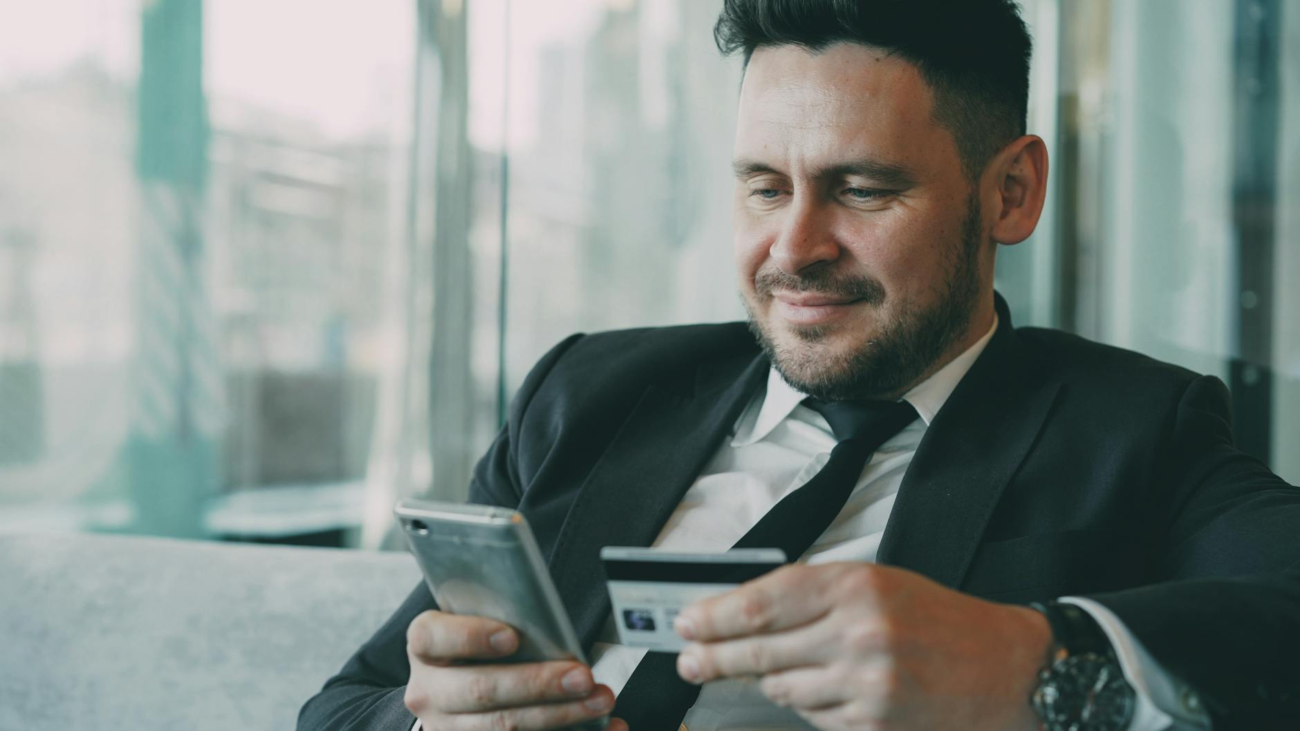 A businessman uses a smartphone and credit card for online shopping in an office setting.