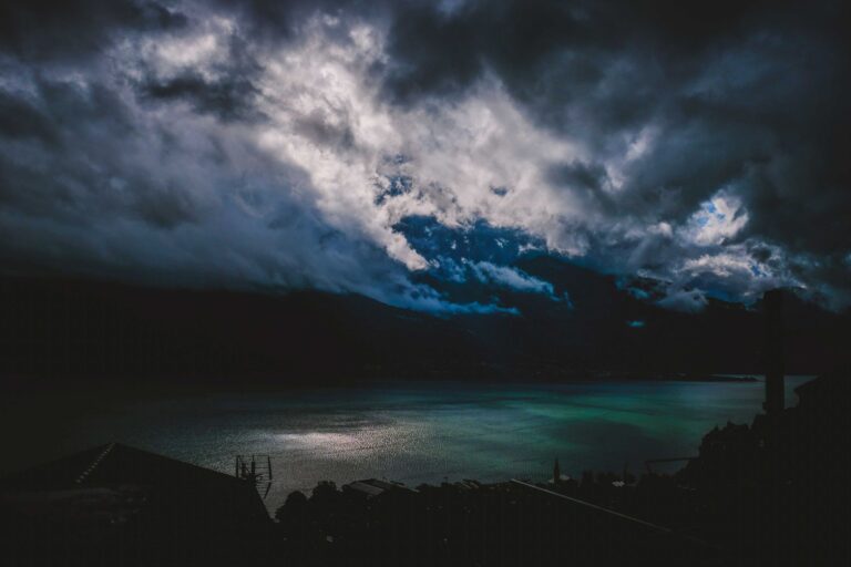 Dramatic view of splendid clouds in sky over lake and building with antenna on coast at night