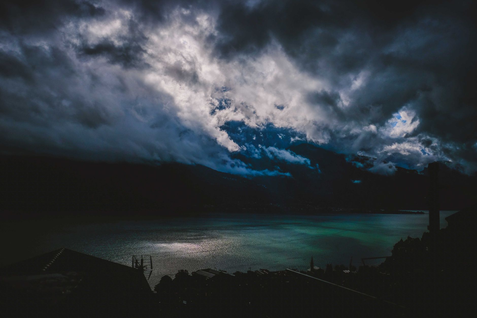 Dramatic view of splendid clouds in sky over lake and building with antenna on coast at night