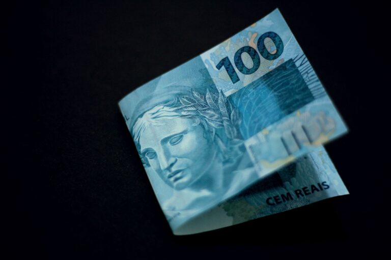 A Brazilian 100 real banknote displayed against a black backdrop, highlighting its design and color.