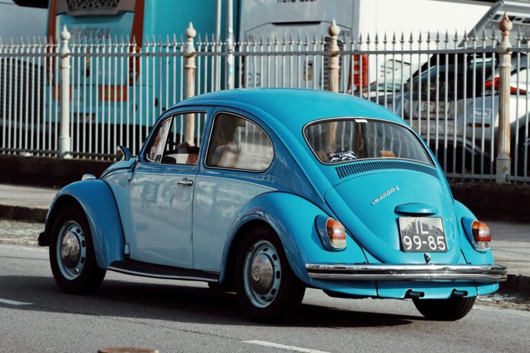 Classic blue Volkswagen Beetle driving on a street in Porto, Portugal, a glimpse of automotive nostalgia.