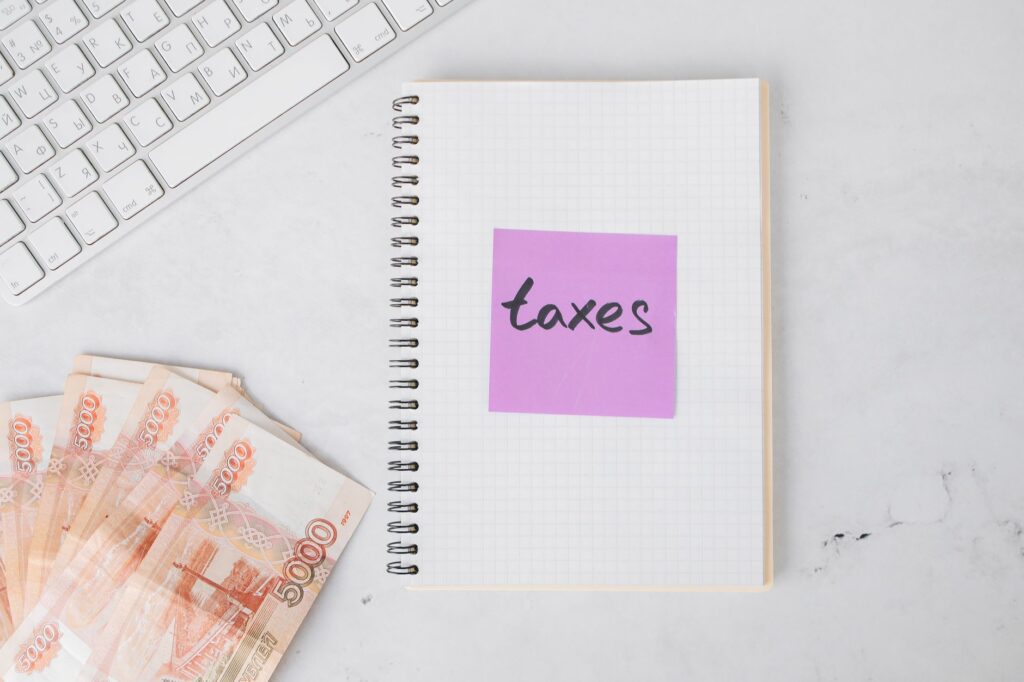 Flat lay image of tax preparation, featuring cash, a notebook, and a computer keyboard on a white surface.