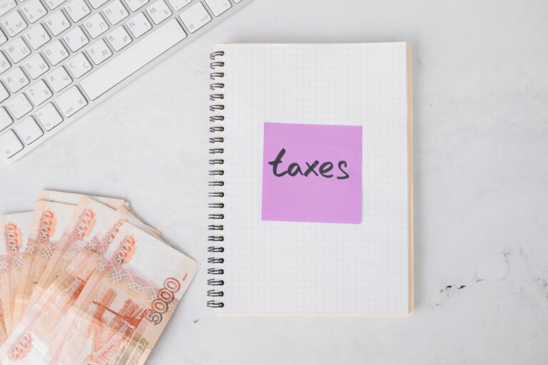 Flat lay image of tax preparation, featuring cash, a notebook, and a computer keyboard on a white surface.