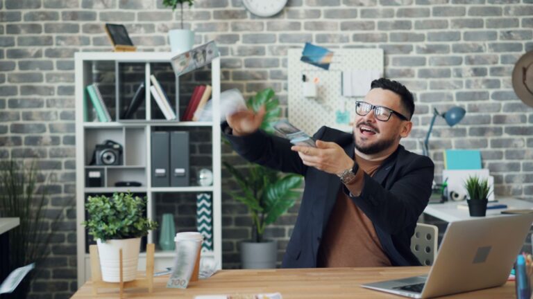 Cheerful businessman in modern office playfully throwing cash, symbolizing financial success and happiness.