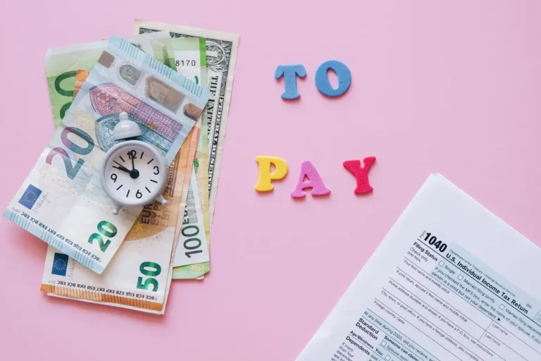 Flat lay of taxes, currency, and reminder to pay on pink background.
