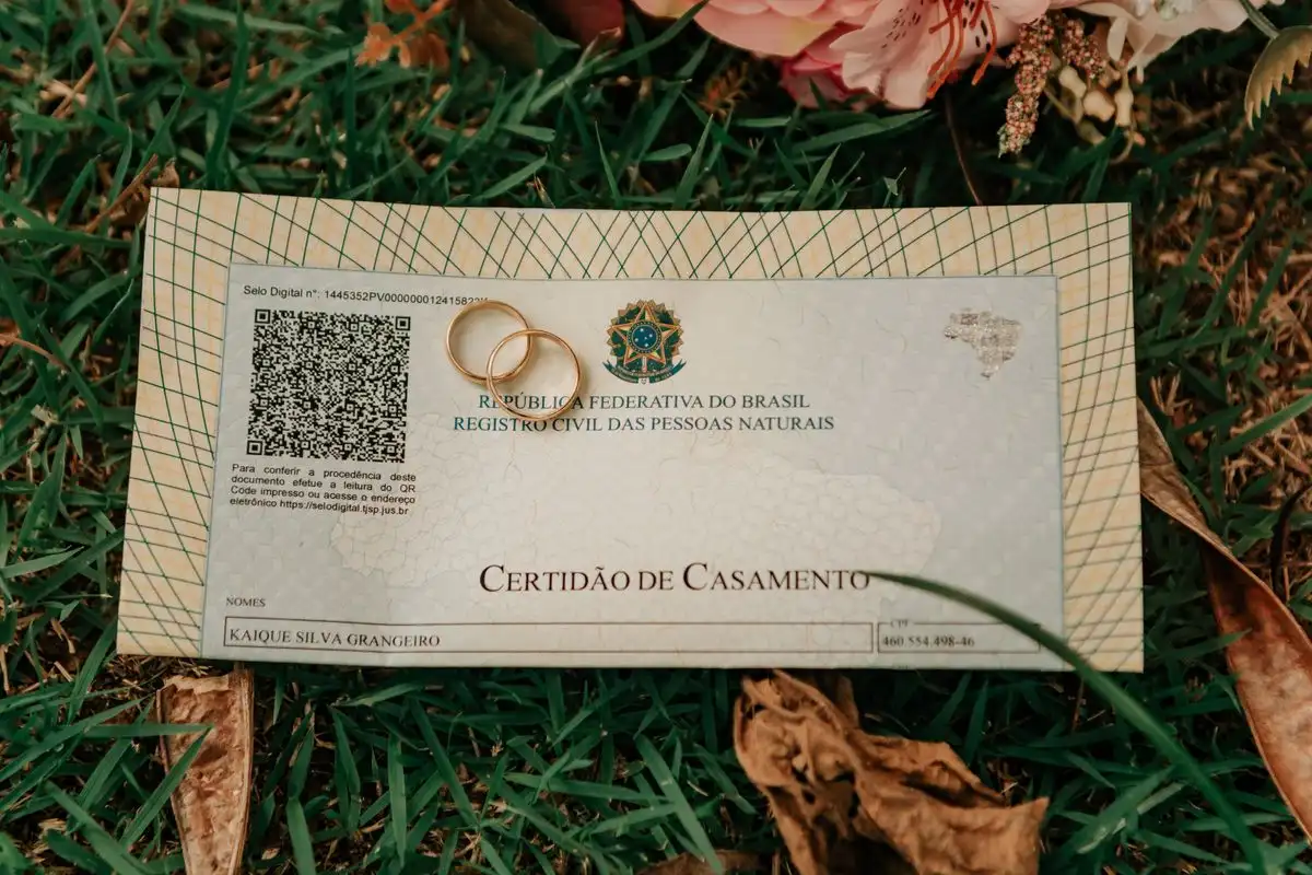 Close-up of a Brazilian marriage certificate with wedding rings and flowers on grass.