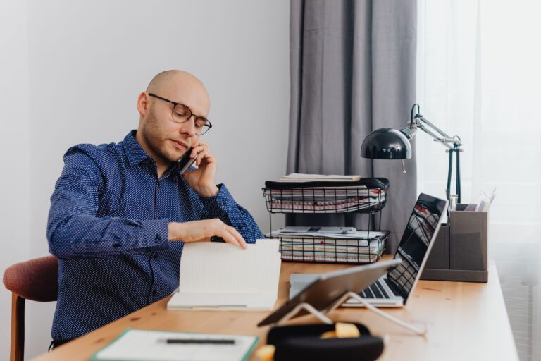 Man working in home office, talking on phone and reviewing notes. Ideal for business or remote work concepts.