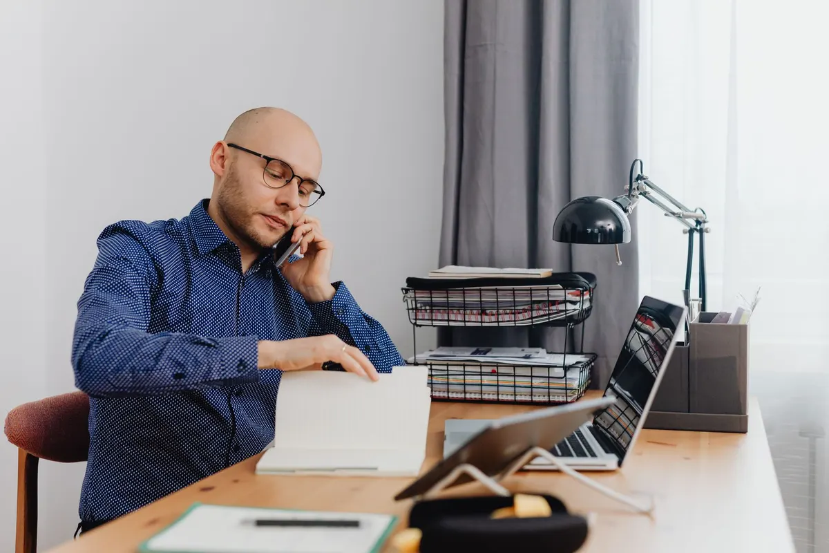 Man working in home office, talking on phone and reviewing notes. Ideal for business or remote work concepts.