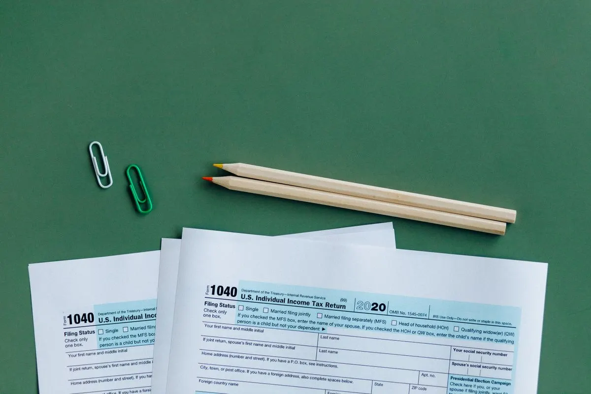 U.S. tax forms with pencils and paperclips on green surface in a flat lay setup.