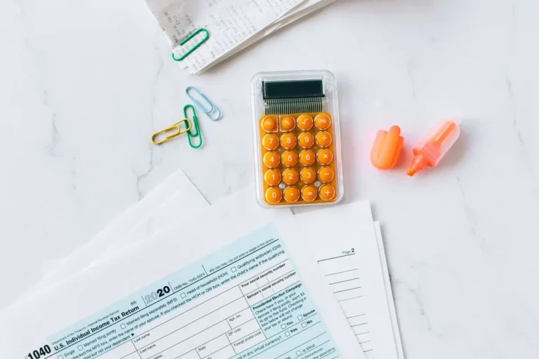 A flat lay image of tax forms, calculator, and office supplies on a desk.