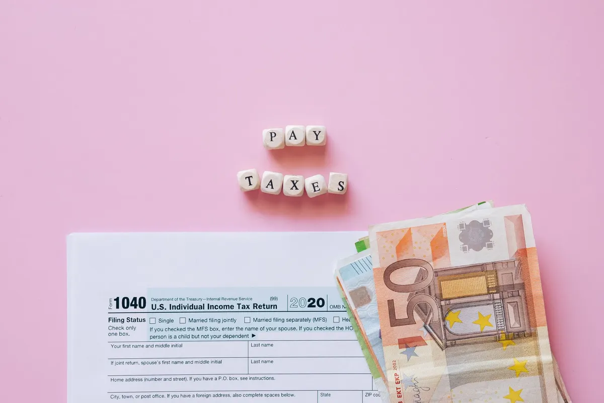 Top view of tax form, euro banknotes, and 'Pay Taxes' letter blocks on pink background.