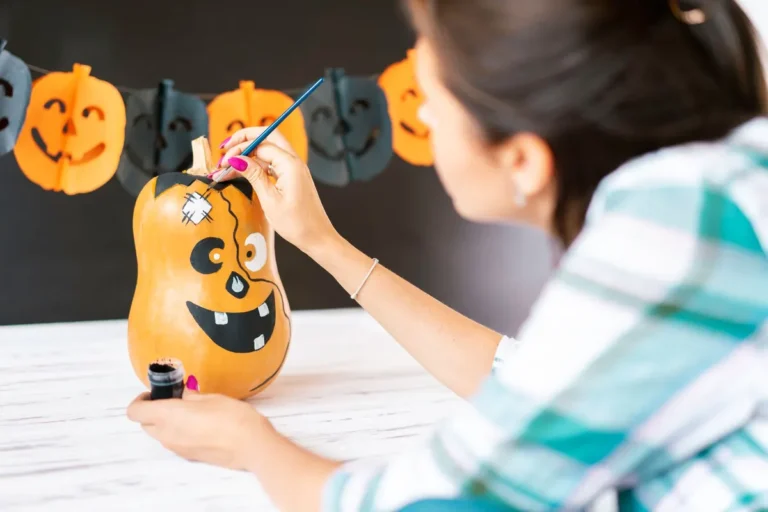 Woman painting a Halloween-themed gourd with decorations in the background.