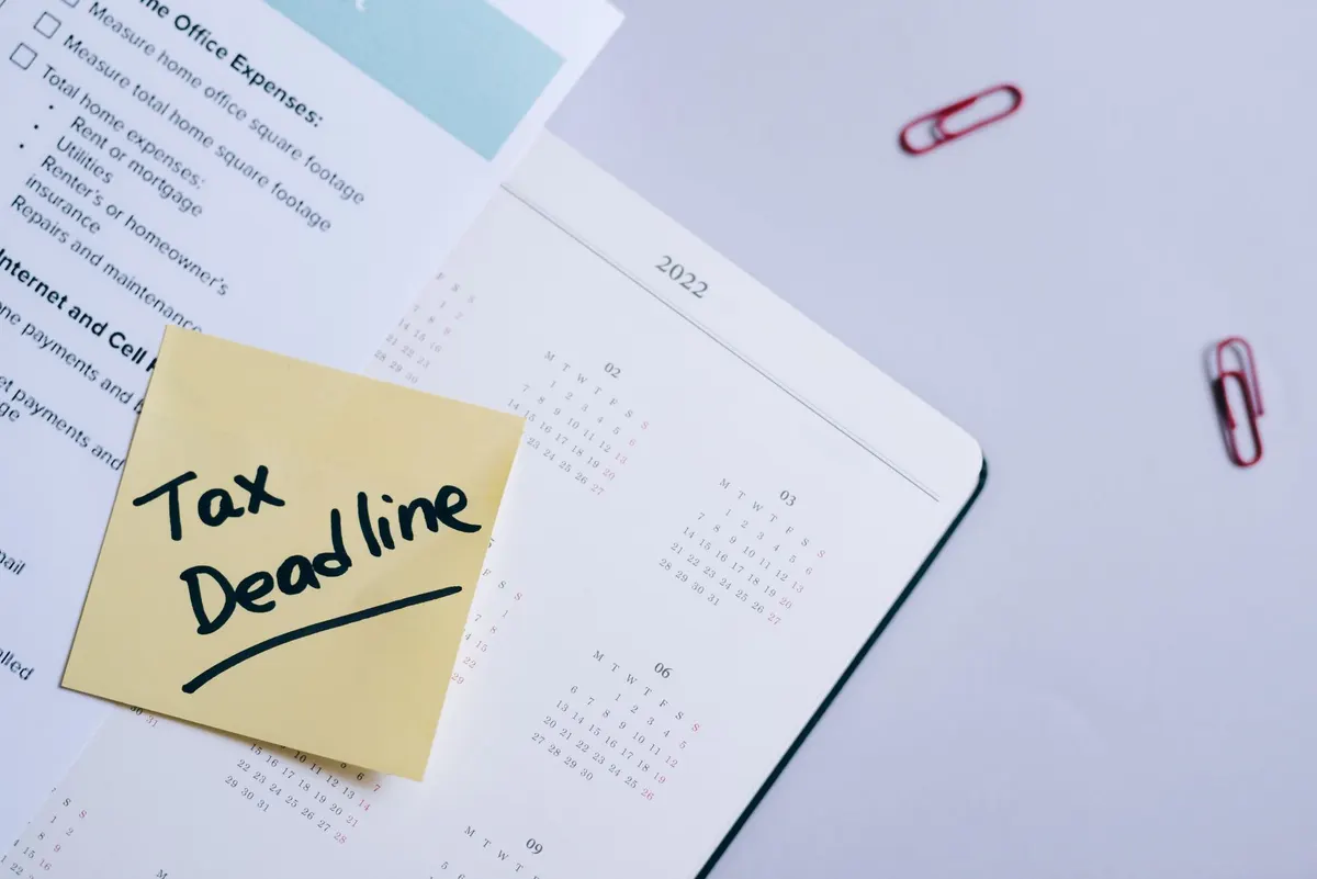 A sticky note highlights tax deadline on a calendar alongside documents, emphasizing financial planning.